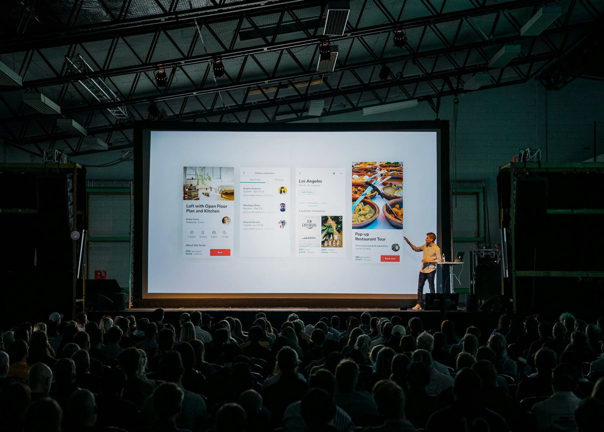 A presenter on stage in front of a large screen and a packed audience