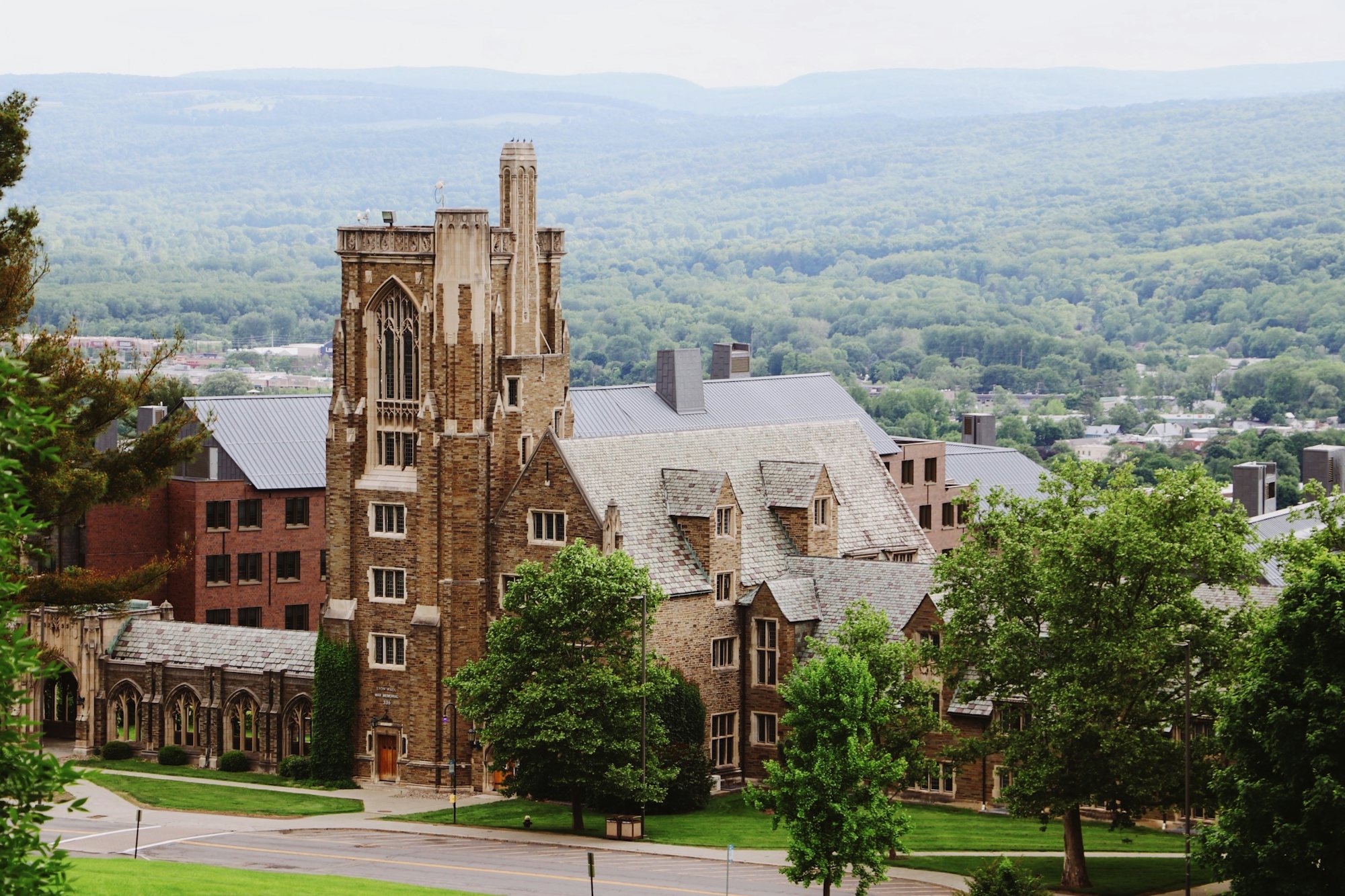 Collegiate Gothic buildings on Cornell's campus framed by summer trees, with hills beyond